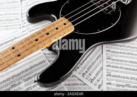 Vintage black bass guitar on music sheets background. Concept of music recording, playing or composing. Close up view. Stock Photo