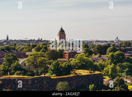 View of Suomenlinna and its old buildings and lighthouse with green trees on a summer day with the Helsinki in the background Stock Photo