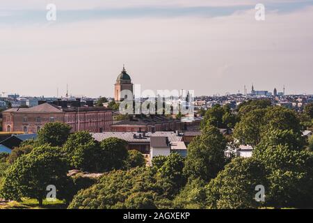 View of Suomenlinna and its old buildings and lighthouse with green trees on a summer day with the Helsinki in the background Stock Photo