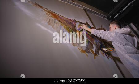 Artist designer draws an eagle on the wall. Craftsman decorator paints picture with acrylic oil color. Painter painter dressed in paint coat. Indoor. Stock Photo