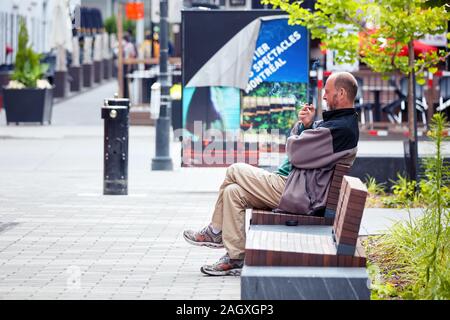 Montreal, Canada - June, 2018: Canadian homeless man sitting on the bench and smoking cigarette. Stock Photo