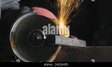 Forge workshop. Smithy manual production. Close up details of sparks, industrial worker using angle grinder and cutting steel. Stock Photo