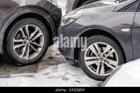 Cars parked with bumpers close to each other, detail on dirty front and tires at snow covered ground. Stock Photo
