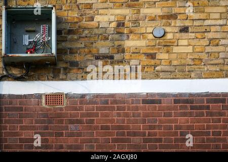 Bricks wall, with electricity / fuse box on it, opened, cover missing, cables visible. Stock Photo