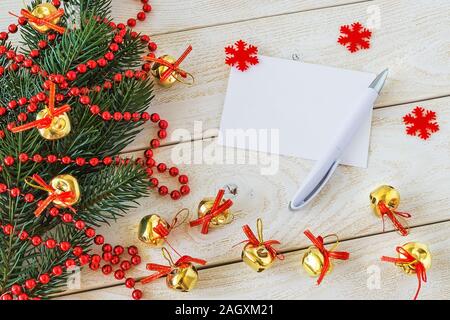 Empty greeteing card and ballpoint pen on a wooden table near a fir branch with red bead garland and golden Christmas balls. Christmas and New Year. Stock Photo