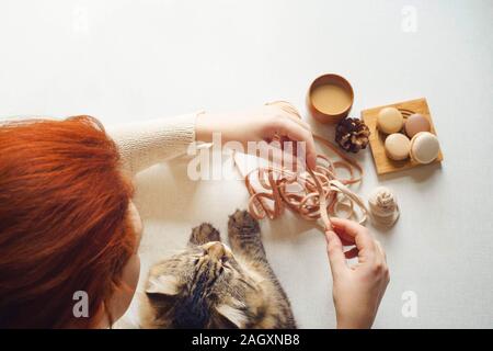 View of the table above where a cat and a girl with red hair drink coffee and unravel a tangle. Spotted kitty and female with red hair drink espresso, Stock Photo