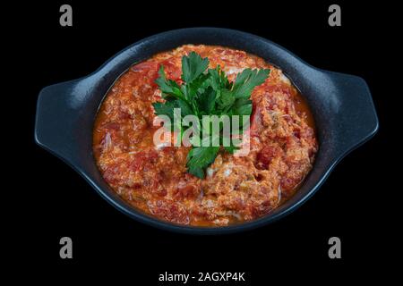 Traditional turkish menemen, made by eggs, tomatoes and various spices. Menemen dinner in cast pan on black background. Stock Photo