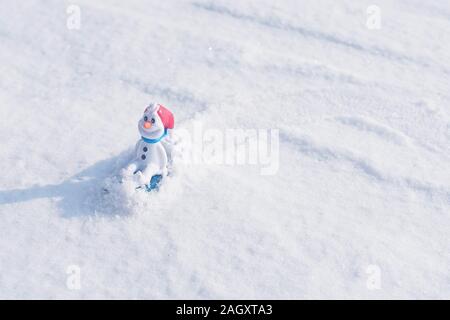 Beautiful snowman on natural snowdrift. Christmas blue background. Snowman toy on the bokeh winter background in the snow. Stock Photo