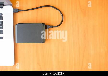 Portable external hard drive on the wooden desk near the laptop for backup your data. Recovery files with hdd. Flat lay with copy space for text Stock Photo