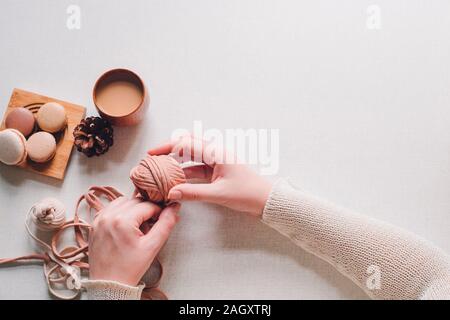 Homemade colorful macarons on the wooden plate on the white background. Female hand is holding yarn. Flat lay with copy space for text Stock Photo