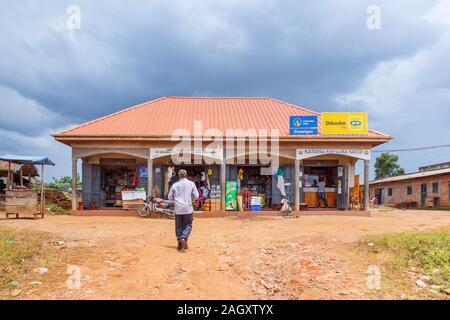 Typical low-rise roadside village shops with a general store shop and buildings with local people in the Western Region of Uganda, on a cloudy day Stock Photo