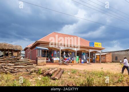 Typical low-rise roadside village shops with a general store shop and buildings with local people in the Western Region of Uganda, on a cloudy day Stock Photo