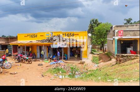 Typical low-rise roadside village shops including a motorcycle repair shop and buildings with local people in the Western Region of Uganda Stock Photo