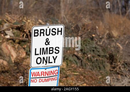 Brush and tree limbs only, no dumping sign at city yard waste disposal, dump site with pile of tree limbs, branches, and leaf bags in background Stock Photo