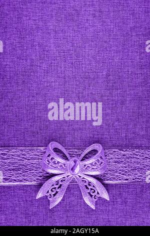 Elegant shiny purple glitter bow on purple colored ribbon and on purple burlap. Vertical greeting card background with large copy space and decorated Stock Photo