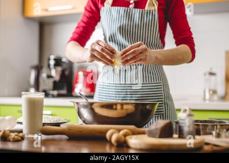 Cook housewife making cookies at home on a colorful kitchen. Woman breaks the eggs in a metal bowl for kneading the dough Stock Photo