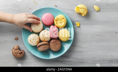 Little, kid's hand reaching for a macaroon from a turquoise plate on a wooden textured table. Copy space Stock Photo