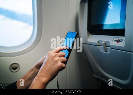 Detail of a woman's hands using mobile phone sitting inside the plane Stock Photo