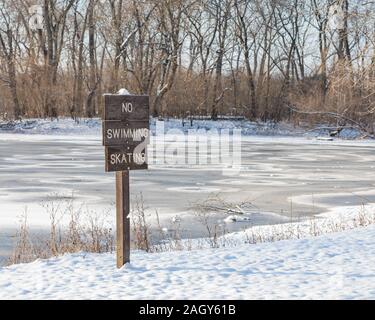 Wooden no swimming, ice skating sign with snow covered ice on frozen lake in background. Concept of winter safety and dangers of thin ice Stock Photo