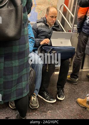 Man already working on his way into work on a New York City subway train. Stock Photo