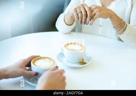 Hands of two young friendly women in casualwear sitting by table in cafe while having cappuccino during conversation at break Stock Photo
