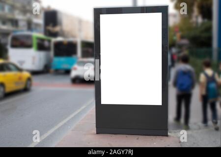 Blank white rectangular billboard at the roadside. On the left comes 2 teenagers on foot. Stock Photo