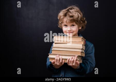 Successful schoolboy holding stack of books while standing in front of camera Stock Photo