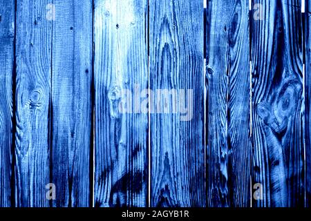 Fragment of burnt and wet old grey wooden fence with rusted screws, knots and openings between planks as a trendy blue background. Main trend of 2020. Stock Photo