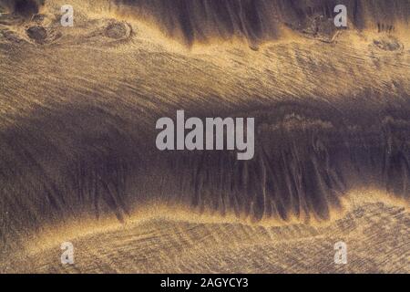 Abstract shapes in wet sand on sea shore, yellow grains with black grains from volcanic ash, zen background, harmony and meditation concept, flat lay Stock Photo