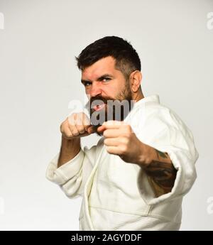 Karate man in kimono hits hand isolated on white background. Athletic kung fu master with beard and raging face practises attack and defence. Martial arts concept Stock Photo