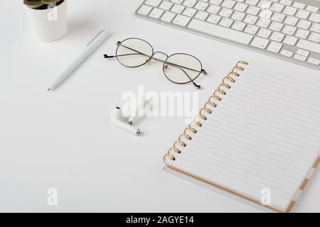 Wireless earphones, eyeglasses, pen, notebook and computer keypad on white desk Stock Photo