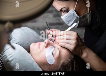 Extensions of artificial eyelash, process close up. Woman in beauty salon. Beauty and self care. Stock Photo