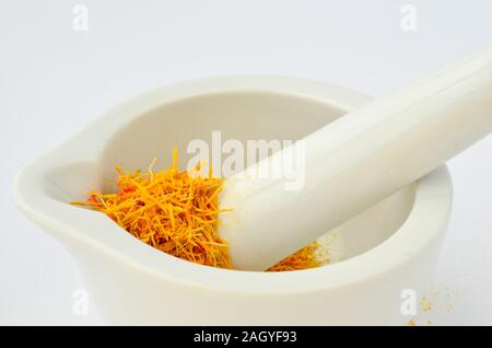 Saffron, tasty and costly spice in white porcelain mortar and wooden teaspoon isolated on white background Stock Photo