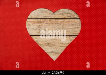 Heart shaped wooden hole torn through paper, isolated on red background. Top view with space for your greetings. Stock Photo