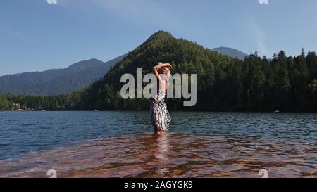 Woman walk on water on pier in sunglasses and a boho silk shawl. Girl rest on flood wood underwater dock. The pavement is covered with water in lake. Stock Photo