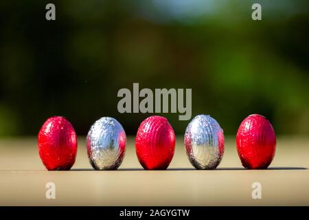 A portrait of five colorful and shiny easter eggs in their wrapping standing up on a table for children to find. Stock Photo