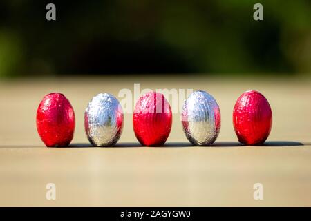 A portrait of chocolate easter eggs wrapped in tin colorful foiln standing up on a table ready to be found and eaten by children. Stock Photo