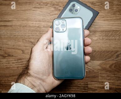 Paris, France - Oct 4, 2019: POV of male hand holding against wooden table background of the new Apple Computers iPhone 11 pro smartphone with clear plastic protection case Stock Photo