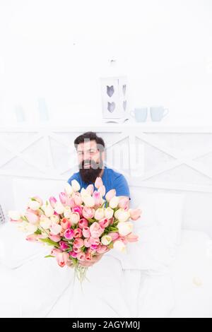 happy bearded man in bed. birthday gift bouquet. spring fresh tulip. love valentines day. womens day. tulip flower for march 8. good morning flowers. positive mood and happiness. Stock Photo