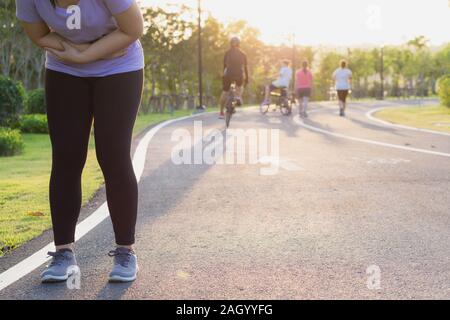 Young woman touching her painful abdominal, suffering from abdominal pain while exercising and running, Sport and exercise concept. Stock Photo