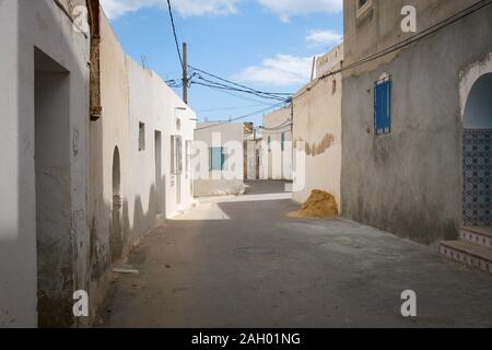 Empty street of Tunisian town in the middle of the day. Buildings with white walls and blue doors and long shadows from midday sun, Hergla, Tunisia Stock Photo