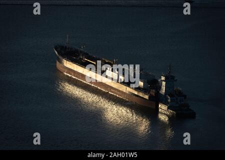 Setting sun reflects off an oil tanker anchored near the head of Burrard Inlet, waiting to take on oil at the western terminus of the TMX pipeline Stock Photo