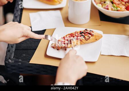 Hands of woman cutting baked bruschetta with knife when having lunch in cafe Stock Photo
