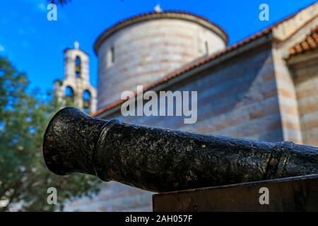 Close up of a barrel of an old cannon with a well preserved wall and church bell tower in the medieval Old town in Budva, Montenegro in the Balkans Stock Photo