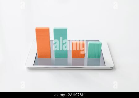 Colorful chart made up of flat wooden bricks standing in row on screen of digital tablet over white background Stock Photo