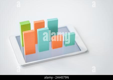 Two rows of blue, orange and green flat wooden bricks making chart on touchpad screen over white background Stock Photo