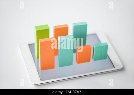 Two rows of flat wooden bricks making colorful chart on screen of digital tablet over white background Stock Photo