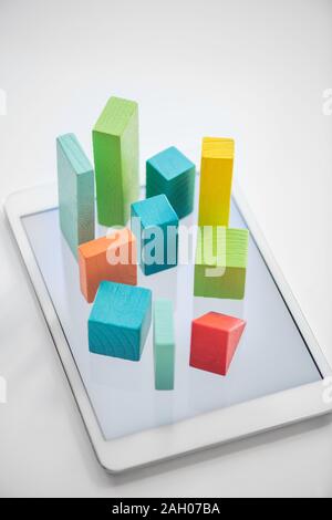 Blue, orange and green flat wooden bricks and cubes symbolizing chart on touchpad screen over white background Stock Photo