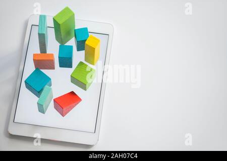 Blue, orange and green flat wooden bricks and cubes making up chart on tablet screen with copyspace on the right Stock Photo