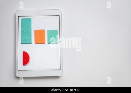 Colorful chart made up of flat wooden bricks lying in row on screen of digital tablet with copyspace on the right Stock Photo